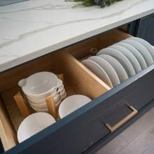 An organized kitchen with a cabinet drawer containing various white bowls and plates.
