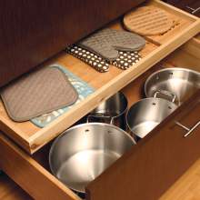 A neatly organized wooden kitchen cabinet containing five pans of various sizes and three oven mitts of different sizes.