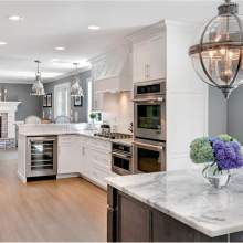 This well-equipped kitchen features white cabinets, marble countertops, appliances, and a decorative potted plant, creating a clean and elegant atmosphere that is perfect for cooking and dining.