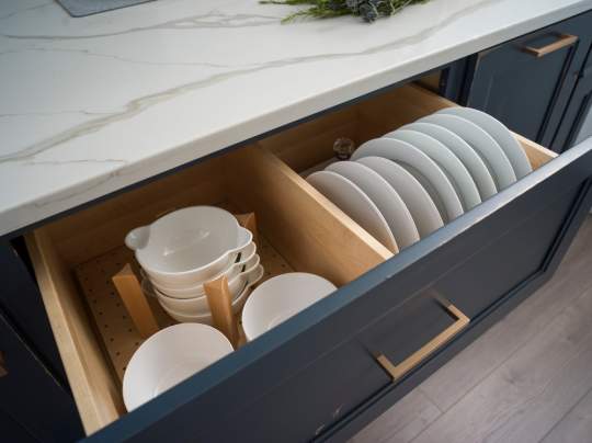 An organized kitchen with a cabinet drawer containing various white bowls and plates.