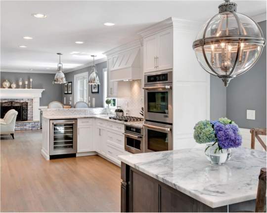 This well-equipped kitchen features white cabinets, marble countertops, appliances, and a decorative potted plant, creating a clean and elegant atmosphere that is perfect for cooking and dining.