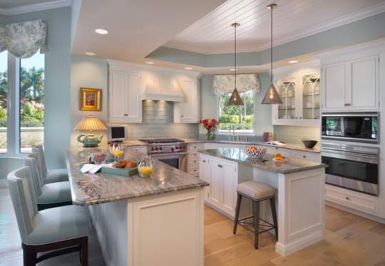 This kitchen is spacious and organized, with an island for food preparation and seating, appliances, and two dining tables, along with some decorative elements. It is both functional and inviting, with a book indicating other activities than just cooking.